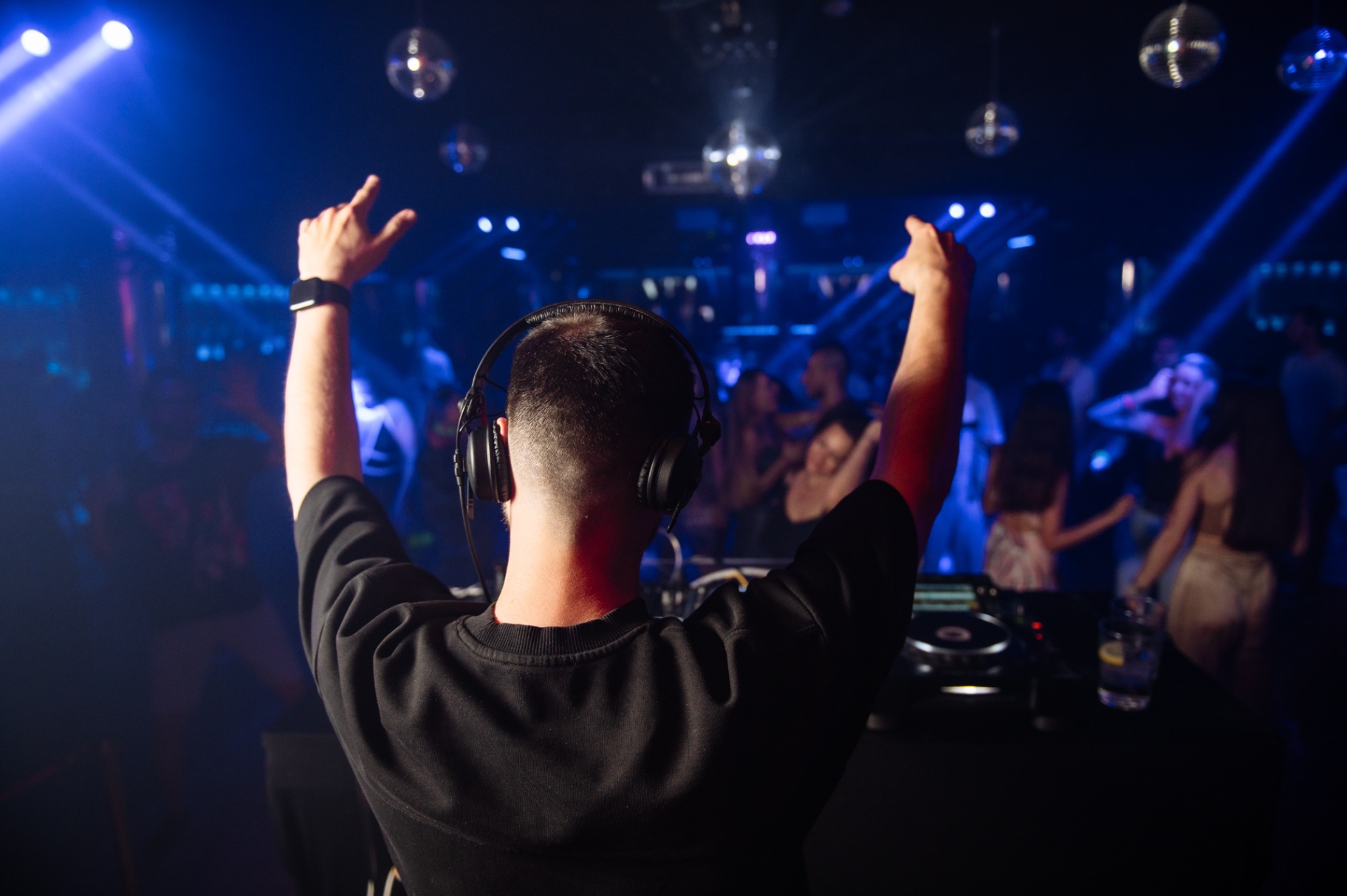 DJ with both hands raised as the floor fills with blue light