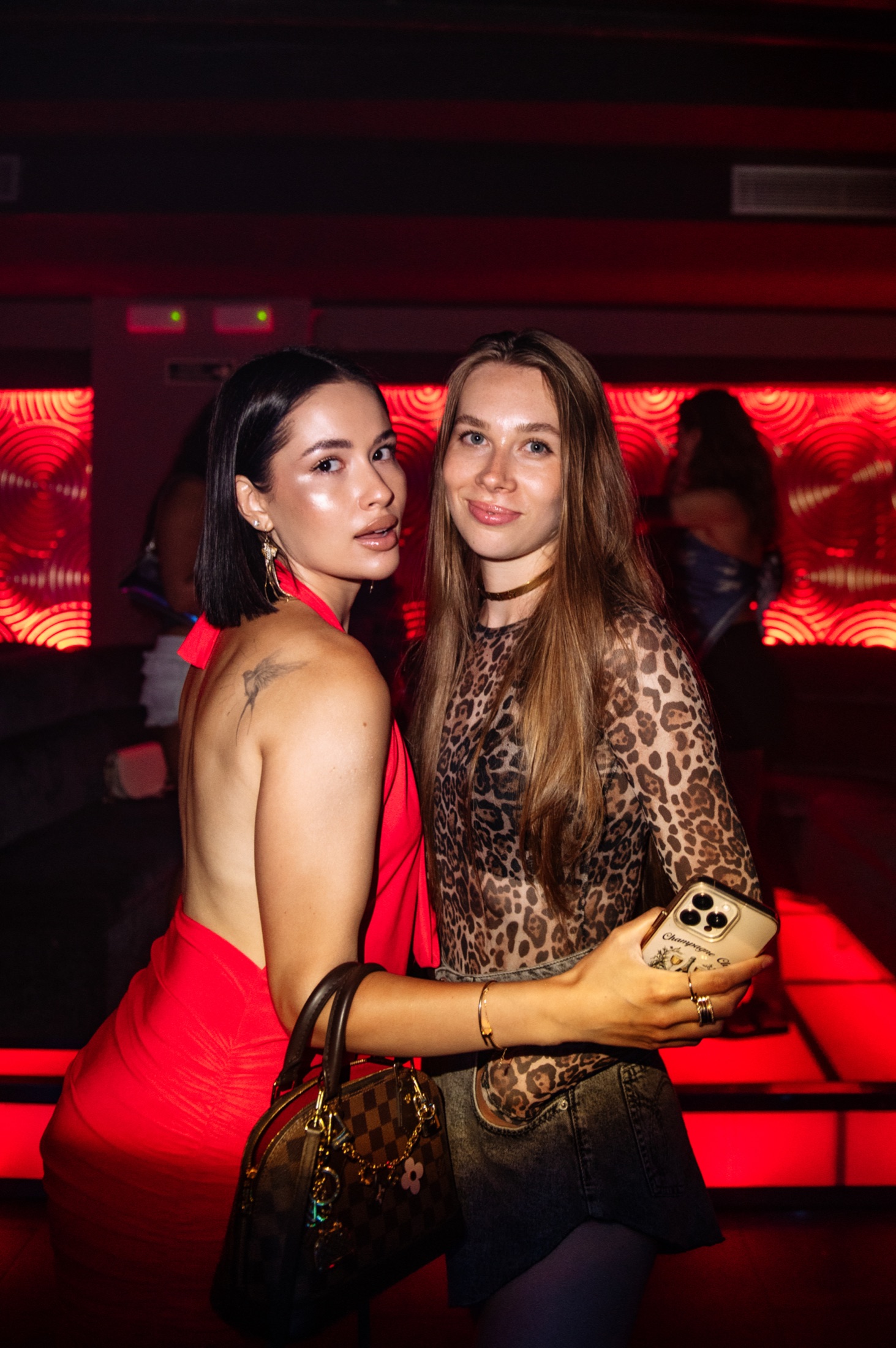 Two guests posing together in the red light of the club